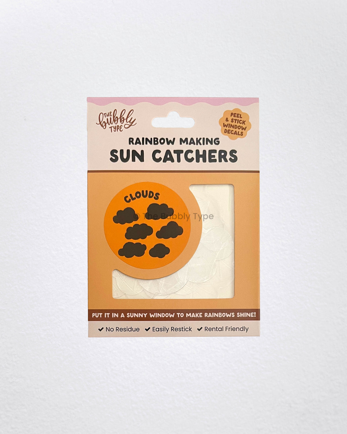 Flat lay of cloud-shaped sun catcher window stickers in The Bubbly Type packaging. Set of six iridescent cloud decals that create rainbows when placed on sunny windows. Australian made, renter-friendly decor – a cute and affordable gift idea for dreamers and cloud lovers.