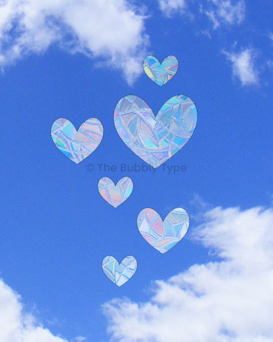 Six heart-shaped sun catchers in various sizes stuck on a window, Australian made rainbow decals spreading love and colour, cute heart window stickers for romantic or playful home decor.