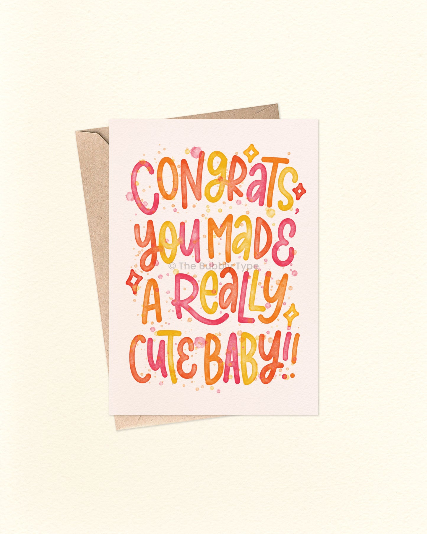 Front of A6 greeting card featuring playful hand-lettered text that reads, “Congrats you made a really cute baby” in warm watercolour tones including red, orange, and yellow. Surrounded by fun starbursts and paint splashes, this cheerful Australian made card by The Bubbly Type is perfect for new parents. Set against a soft cream background and shown with a brown kraft envelope.