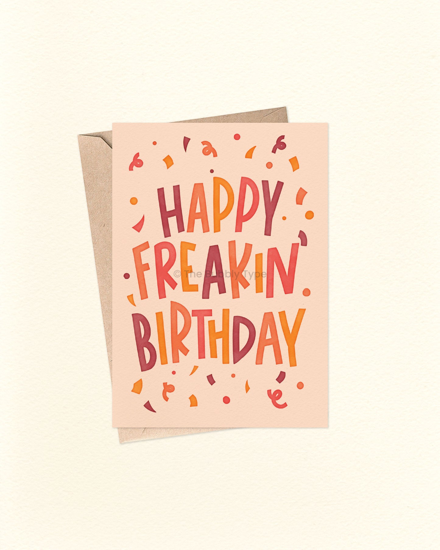 Front of A6 birthday card featuring bold blocky hand-lettered text that reads “Happy Freakin' Birthday” surrounded by colourful confetti. The design uses warm, bright colours like orange, yellow, warm purple, and cream. A fun and cheeky birthday card from The Bubbly Type, perfect for friends or anyone who loves bold vibes. Shown with a brown kraft envelope.