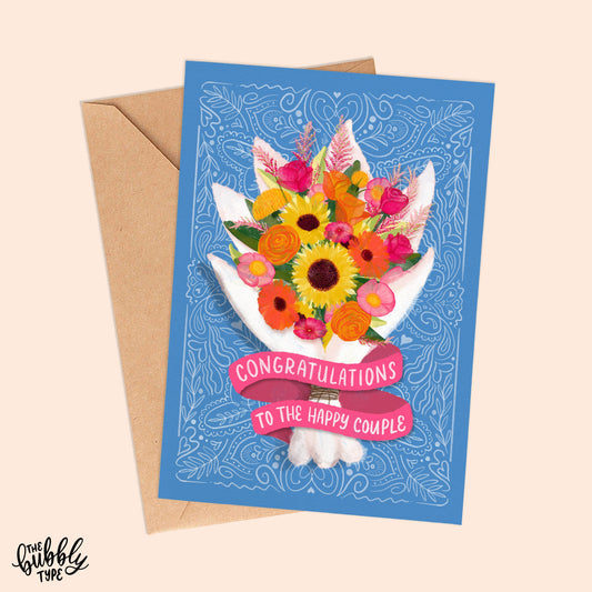 Australian made wedding cards and engagement cards. Congratulations to the happy couple bouquet of flowers. Front of A6 card designed for weddings or engagements. The background is a soft blue with fine white line pattern details. A vibrant watercolour-style bouquet takes centre stage, featuring sunflowers, hot pink and orange roses, pink peonies, yellow roses, and green foliage. The flowers are wrapped in a white paper wrap, with a pink ribbon banner at the bottom that reads: “Congratulations to the happy