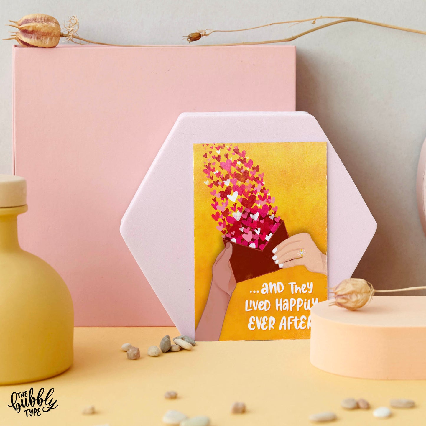 Australian Made Wedding and Engagement Cards. And they lived happily ever after in love. Front of A6 wedding card featuring a yellow watercolour background with a hand-drawn illustration of two different hands holding a red envelope. One hand wears a diamond engagement ring. A joyful burst of red love hearts rises from the envelope. At the bottom, bold white hand-lettered text reads: “... and they lived happily ever after.” Use as a wedding card or an engagement party card. Congratulations on your wedding.