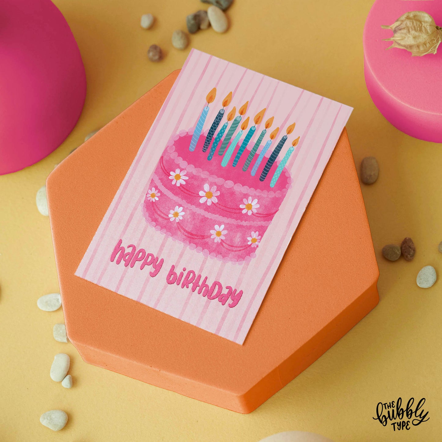 Australian made Happy Birthday Greeting Cards. Cute card for her. Front of A6 birthday card featuring a whimsical illustration of a pink cake topped with white daisy icing flowers and a cluster of blue and teal candles. Hand-lettered “Happy Birthday” sits below the cake on a pale pink background with soft watercolor line textures.
