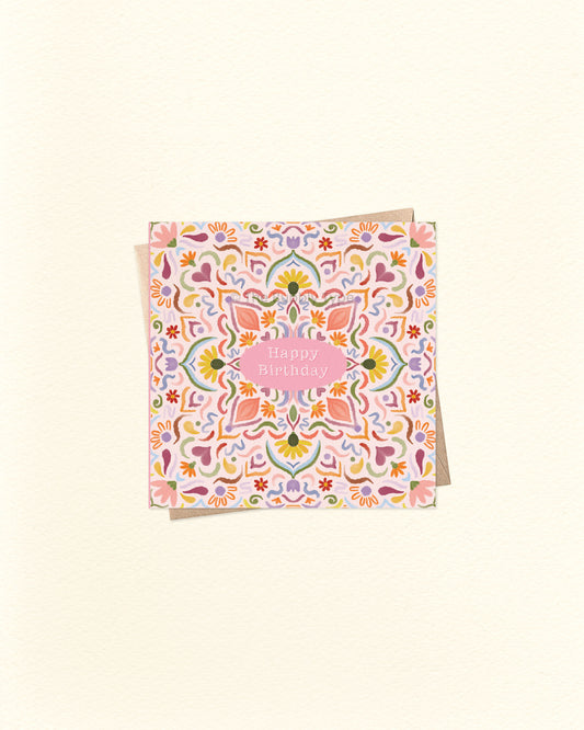 Front of 10cm square birthday card featuring a watercolour tile pattern in warm, vibrant colours – including pink, orange, blue, and purple. “Happy Birthday” is written in small text at the centre. Paired with a brown kraft envelope. A colourful and artistic Australian made birthday card by The Bubbly Type.