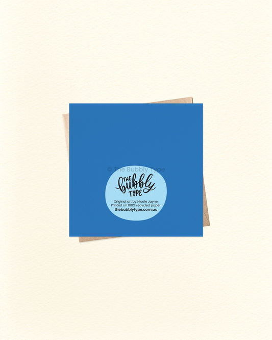 Back of the new baby greeting card with deep blue background, showing The Bubbly Type logo and print details. Printed in Australia on sustainably sourced cardstock. Shown over a kraft brown envelope.