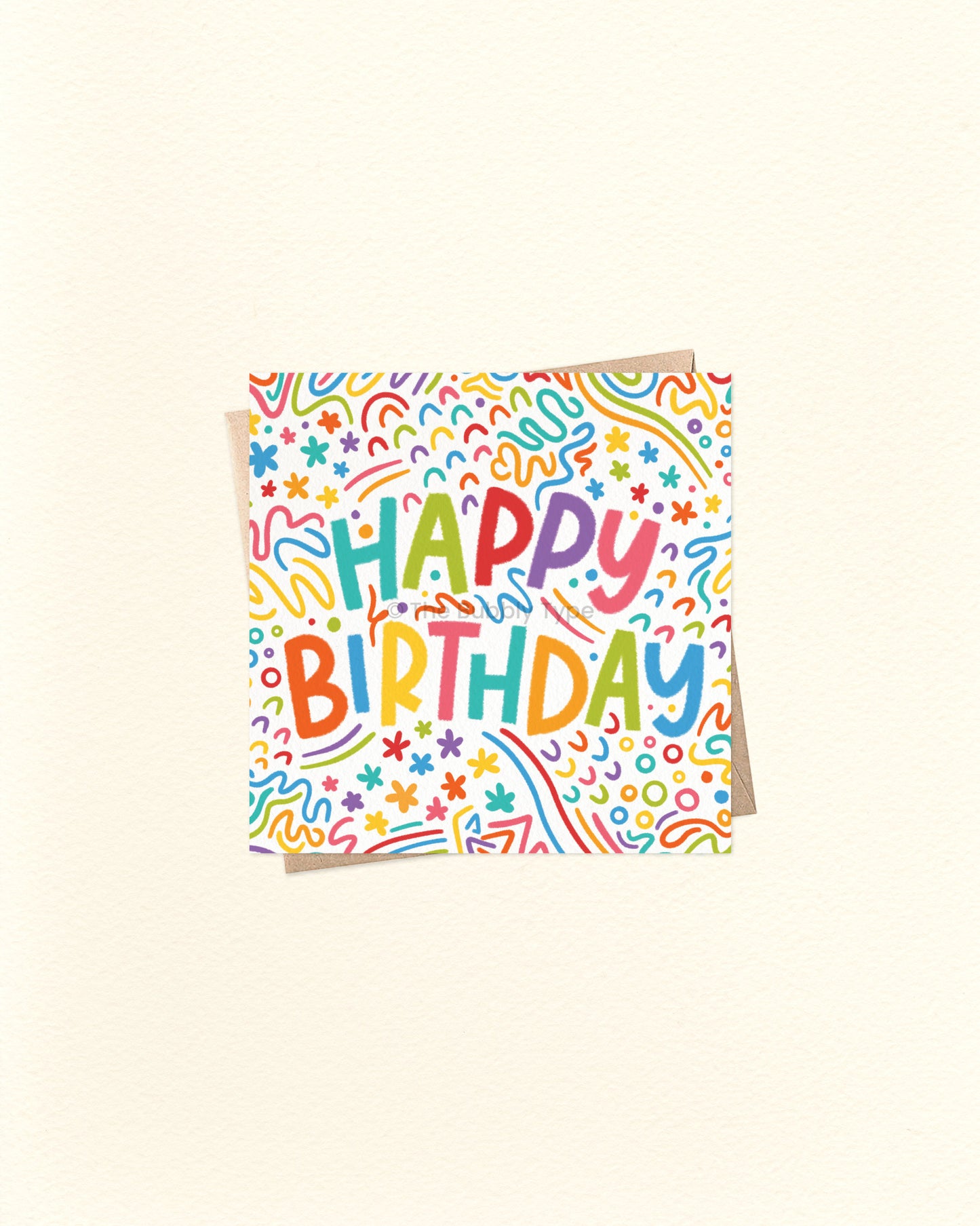 A square birthday card with a white background covered in colourful doodle patterns and the words 'HAPPY BIRTHDAY' in playful multicoloured lettering, shown on a warm off-white background.