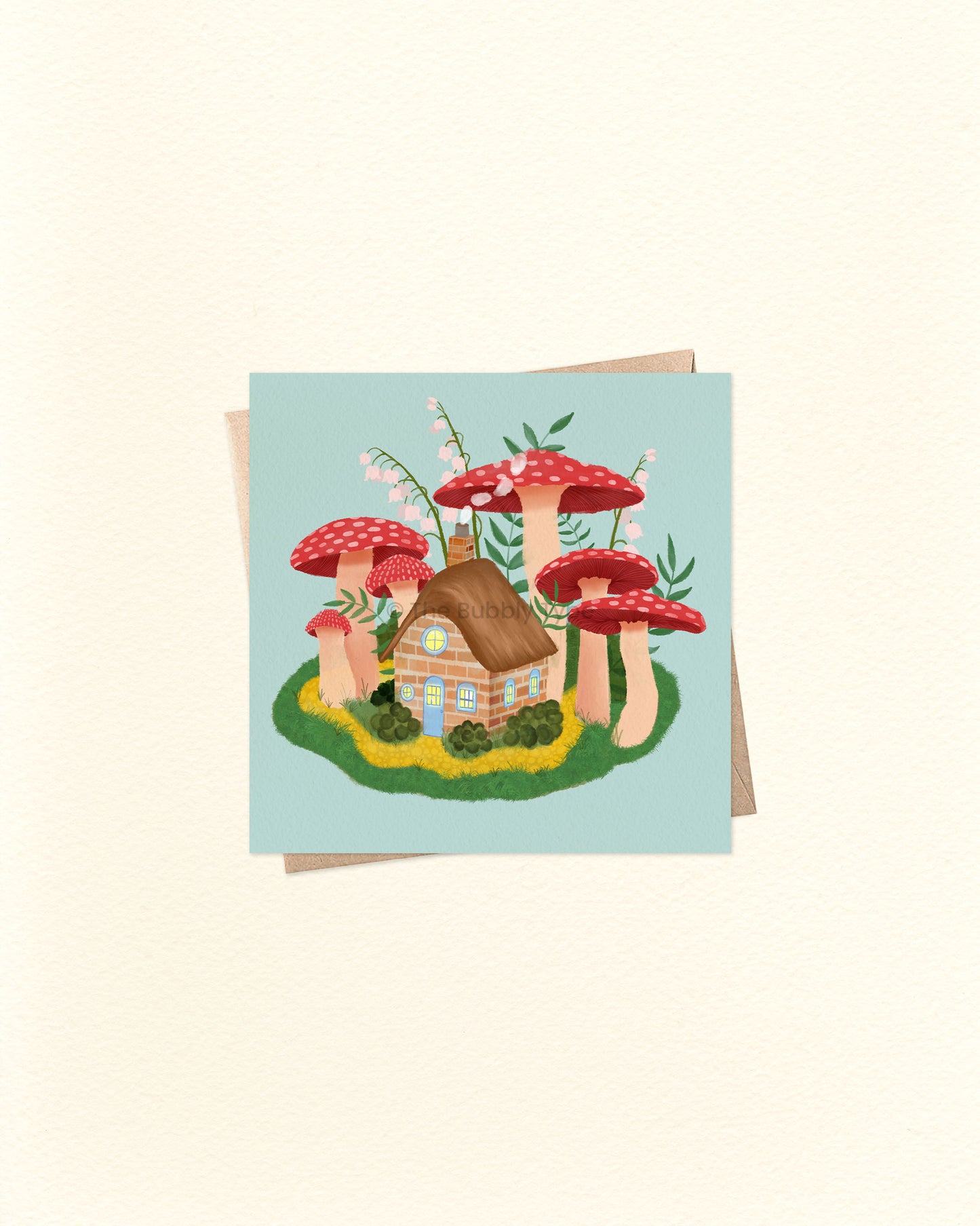 Front of square greeting card featuring a whimsical illustration of a cottage surrounded by mushrooms, paired with a brown kraft envelope. 10cm x 10cm card by The Bubbly Type – Australian made and blank inside. Perfect for fairytale lovers, nature fans, or a magical little note.