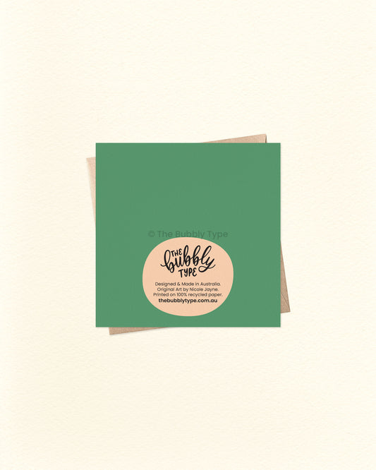 Back of the 10cm square Mushroom Cottage card with green background, showing The Bubbly Type logo and printed details, placed over a kraft brown envelope. Designed and printed in Australia on eco-friendly cardstock.