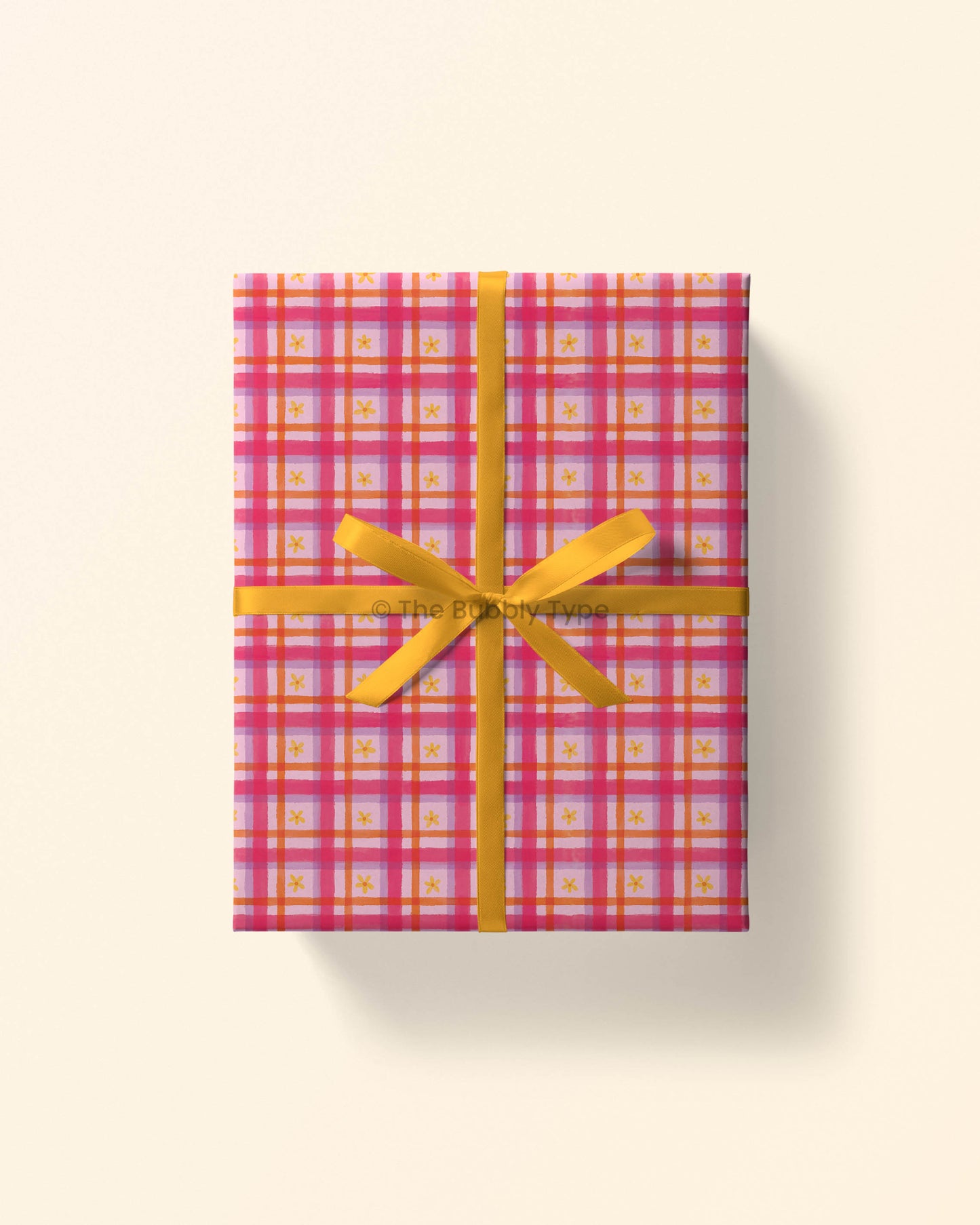 Top view of a gift wrapped in pink daisy gingham wrapping paper, showing yellow daisies on a pink checkered pattern. Perfect gift wrap for girls and friends to celebrate birthdays or any fun occasion.