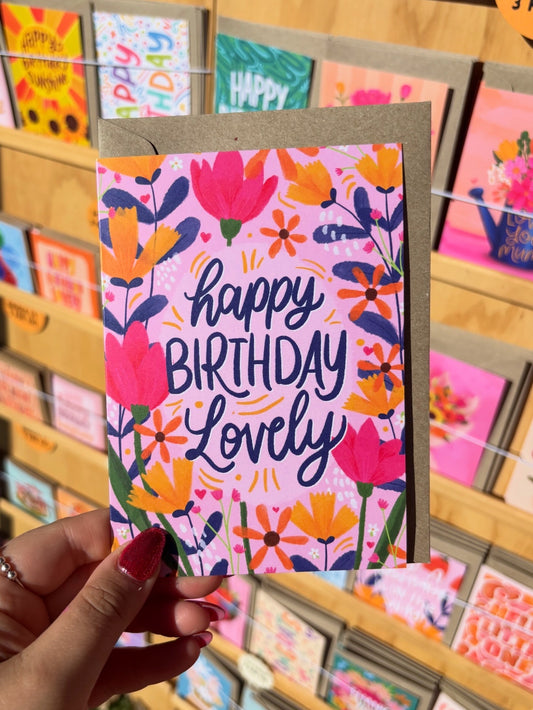 Hand holding a colorful birthday card with floral design and 'Happy Birthday Lovely' text.