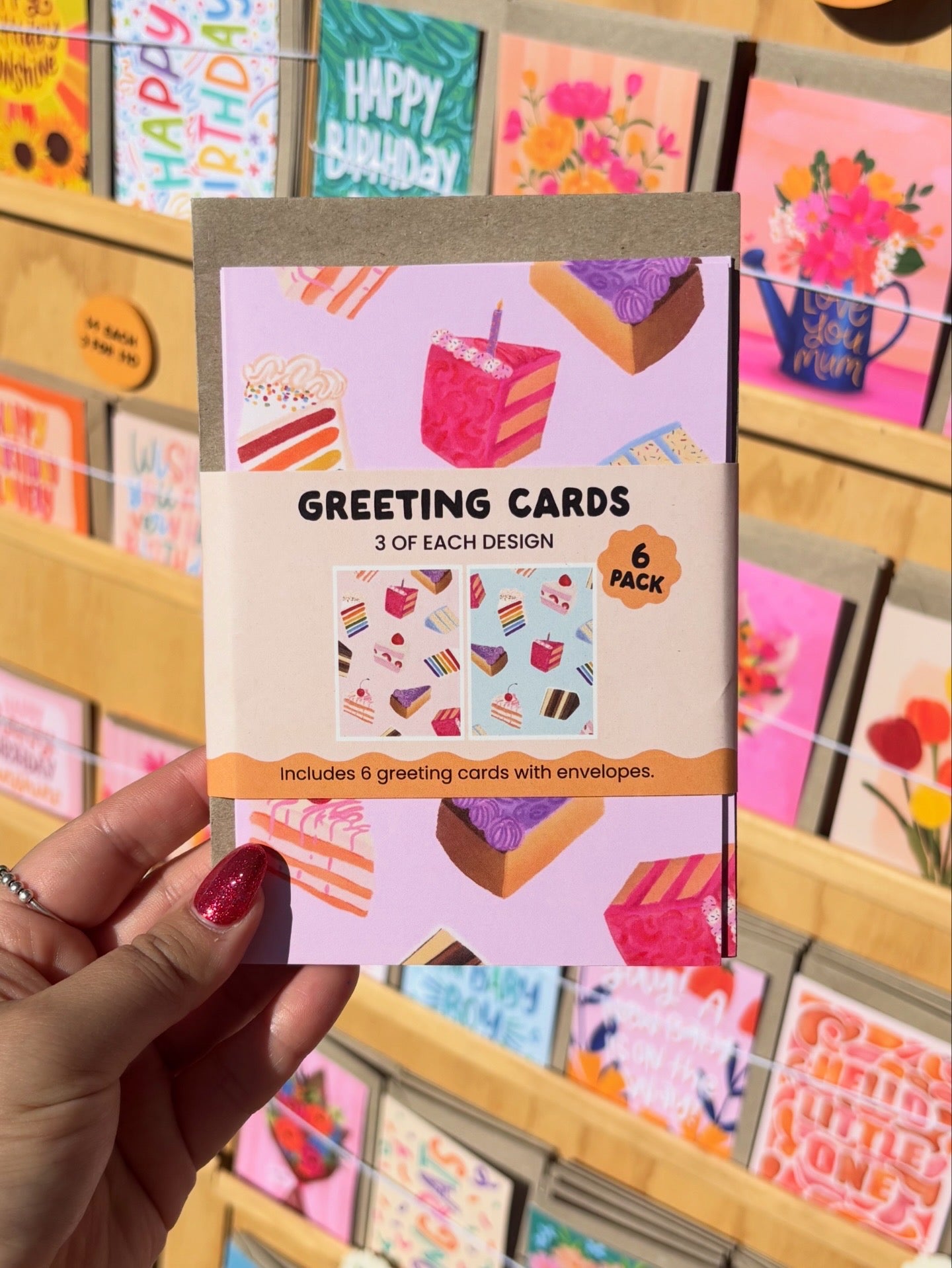 Pack of greeting cards held by a hand with a colourful background of more cards.