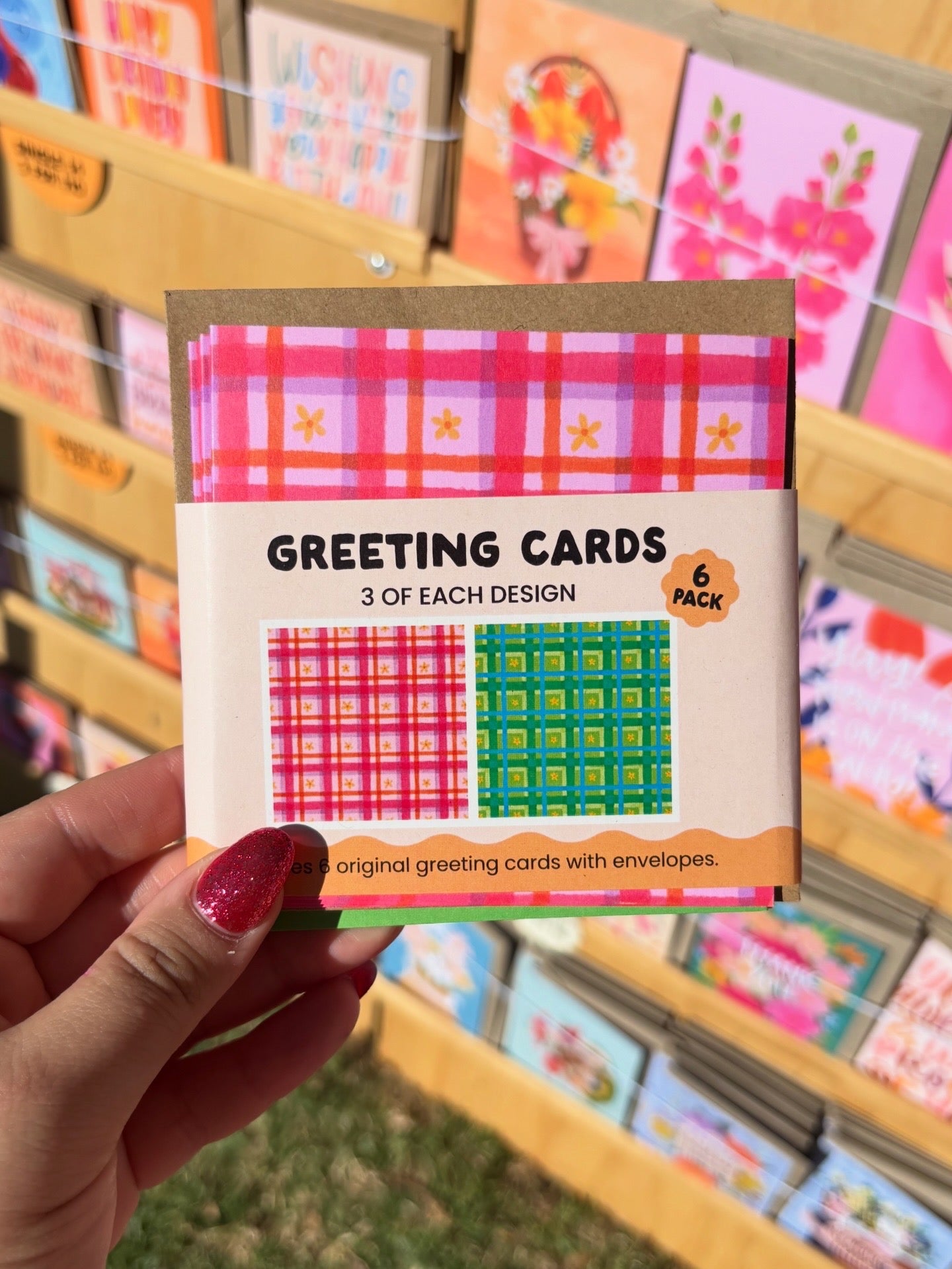 Pack of greeting cards with a hand holding it, set against a background of more greeting cards.