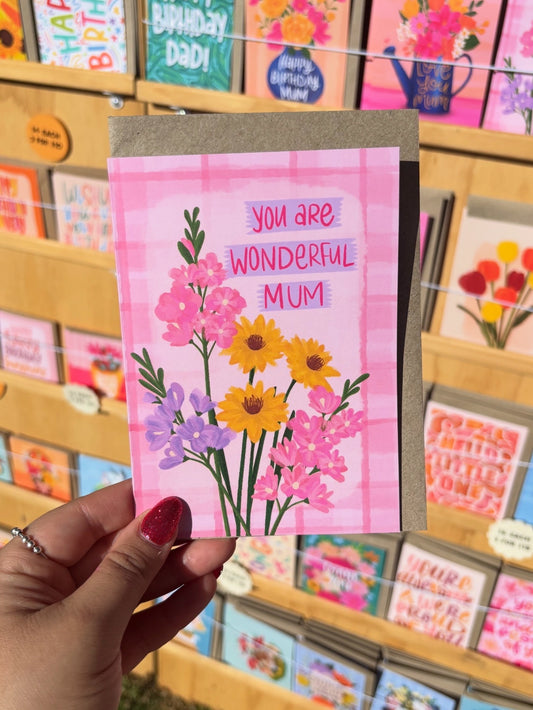 Hand holding a card with flowers and 'You are wonderful mum' text in front of a display of other cards.