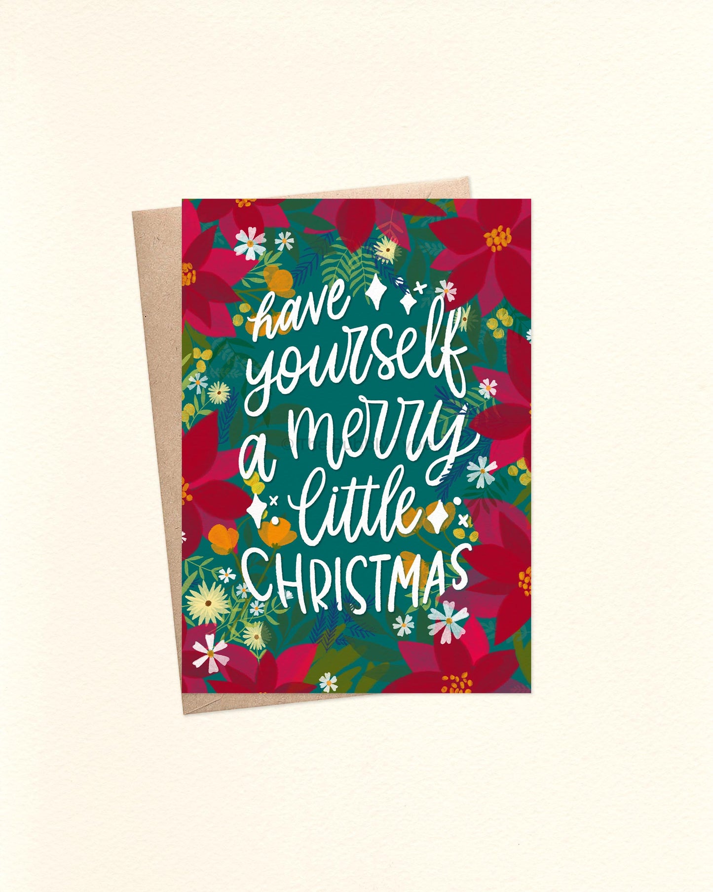 A6 Christmas card featuring the message “Have yourself a merry little Christmas” in white hand lettering, centred on a deep green background. Surrounding the text are illustrated red poinsettias, green foliage, and small white and yellow flowers in a watercolour style. A brown kraft envelope sits behind the card.