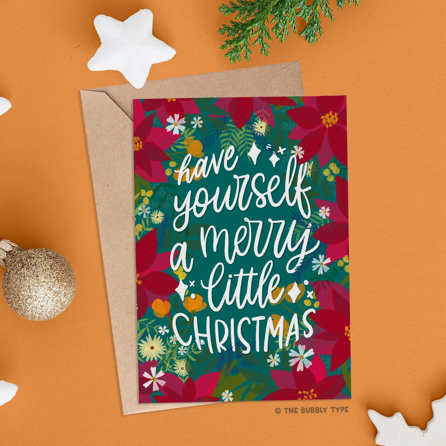 The card is shown on an orange background surrounded by sparkly gold baubles and white glittery star ornaments, creating a festive holiday setting. Australian made Christmas cards. Have yourself a merry littler christmas, hand drawn design. Affordable Christmas gift card