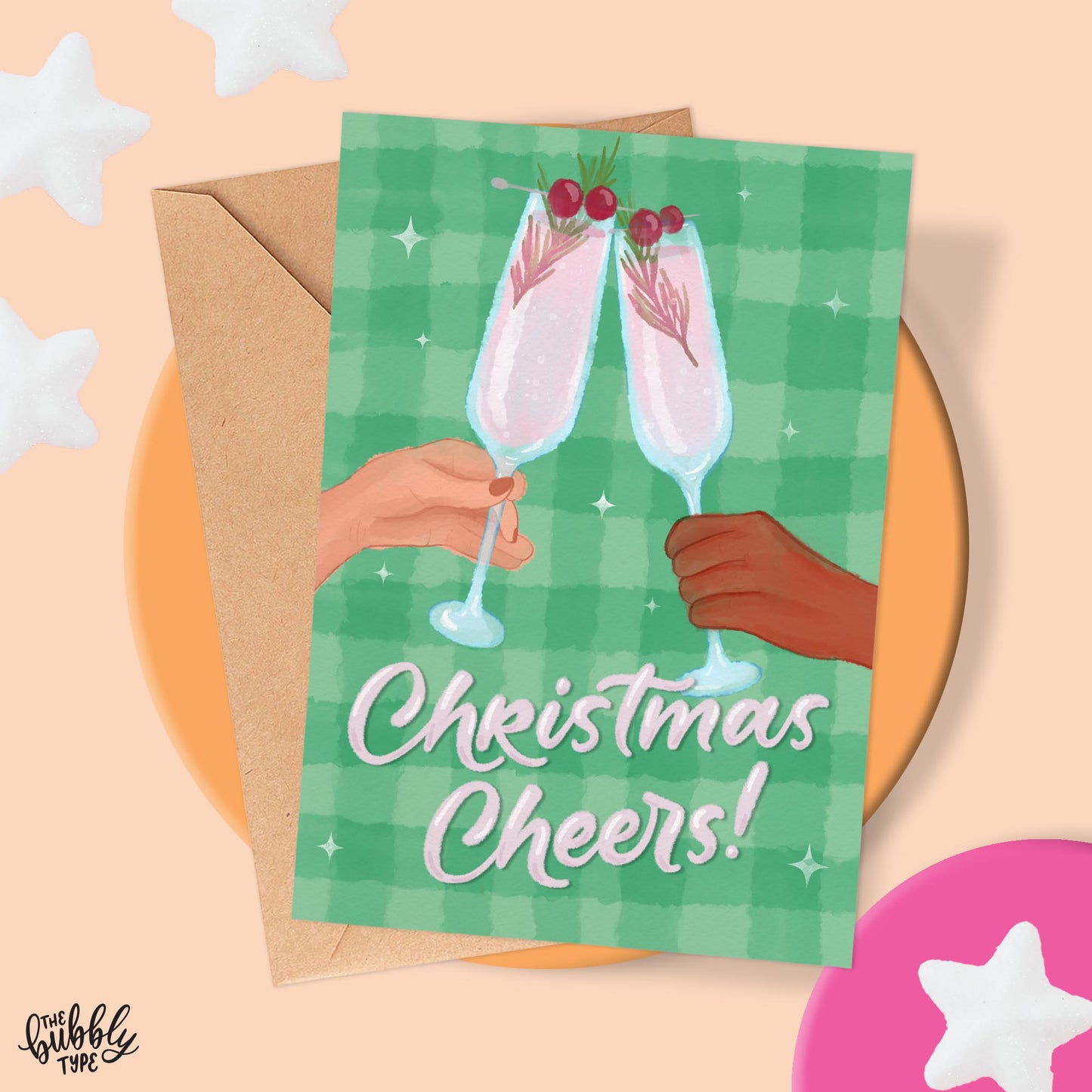 Christmas Cheers Greeting Card with hands holding champagne flutes together in a celebratory cheers gesture. Green plaid background and hand lettered words"Christmas Cheers" round out the Design. Best handmade Christmas cards made in Australia.