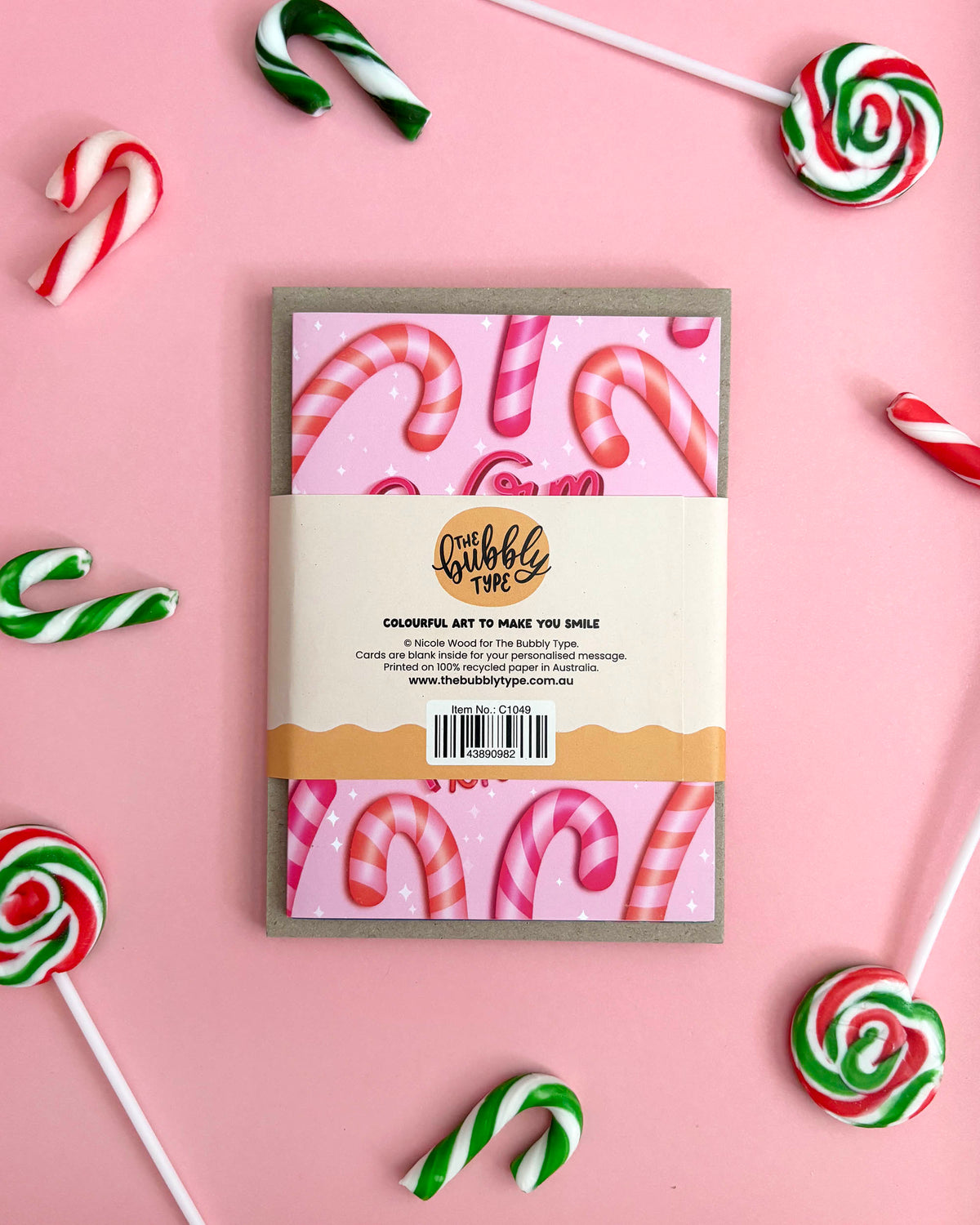 The back of a Christmas-themed greeting card pack styled in a flat-lay with candy canes and lollipops on a pink background.