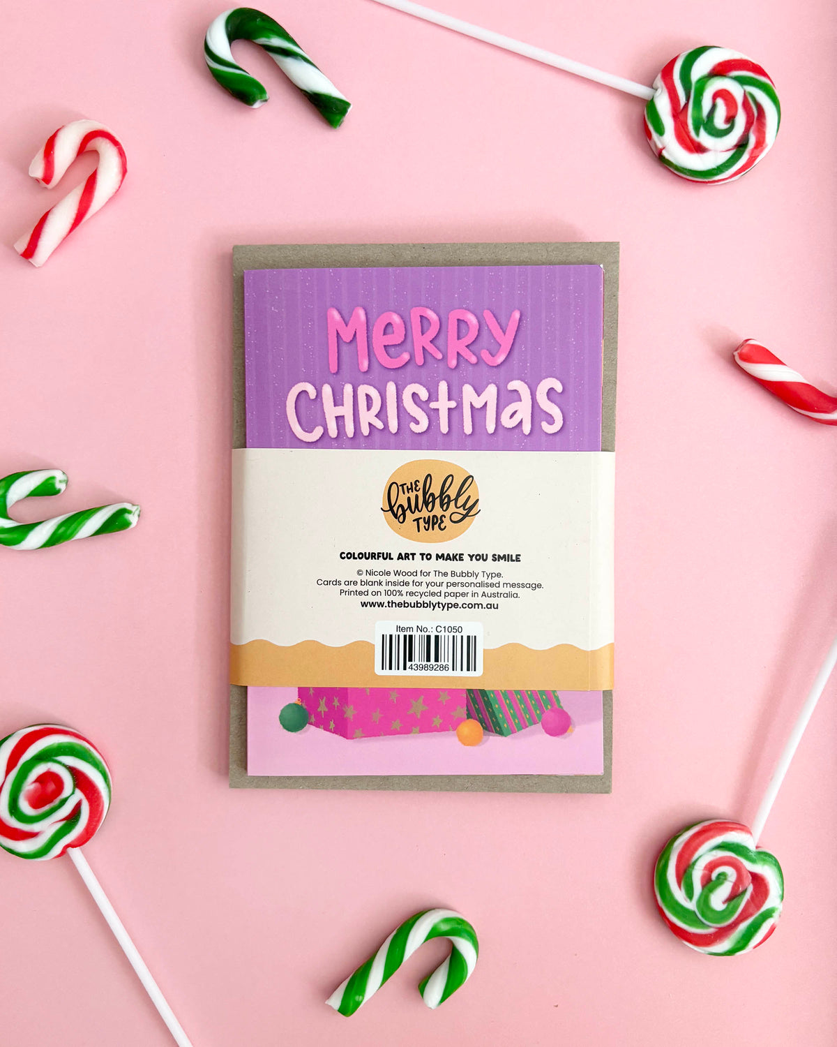 The back of a Christmas-themed greeting card pack styled in a flat-lay with candy canes and lollipops on a pink background.