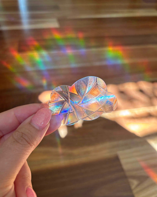 Iridescent Sun Catcher Sticker held by a hand with rainbow lights in the background.