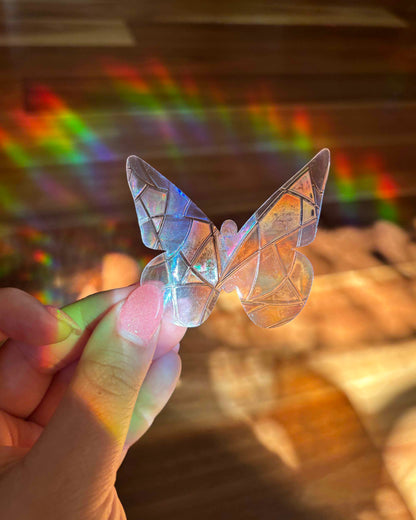 Butterfly-shaped sun catcher sticker with iridescent colours held by a hand against a blurred background with rainbow light.