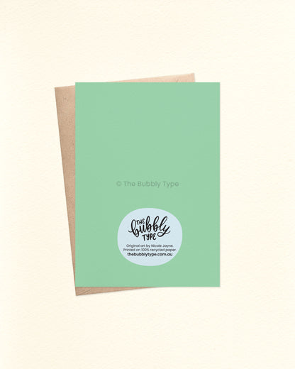 Back of the card featuring a pale green background with The Bubbly Type logo and card details. Shown with a kraft brown envelope.