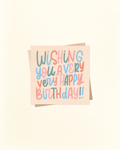 Front of 10cm square birthday card with hand-lettered text reading “Wishing You a Very Very Happy Birthday!!” in whimsical lettering. Features a colour palette of green, blue, orange, and pale pink on a soft orangey beige background. Paired with a brown kraft envelope. A fun and playful birthday card by The Bubbly Type – proudly Australian made.