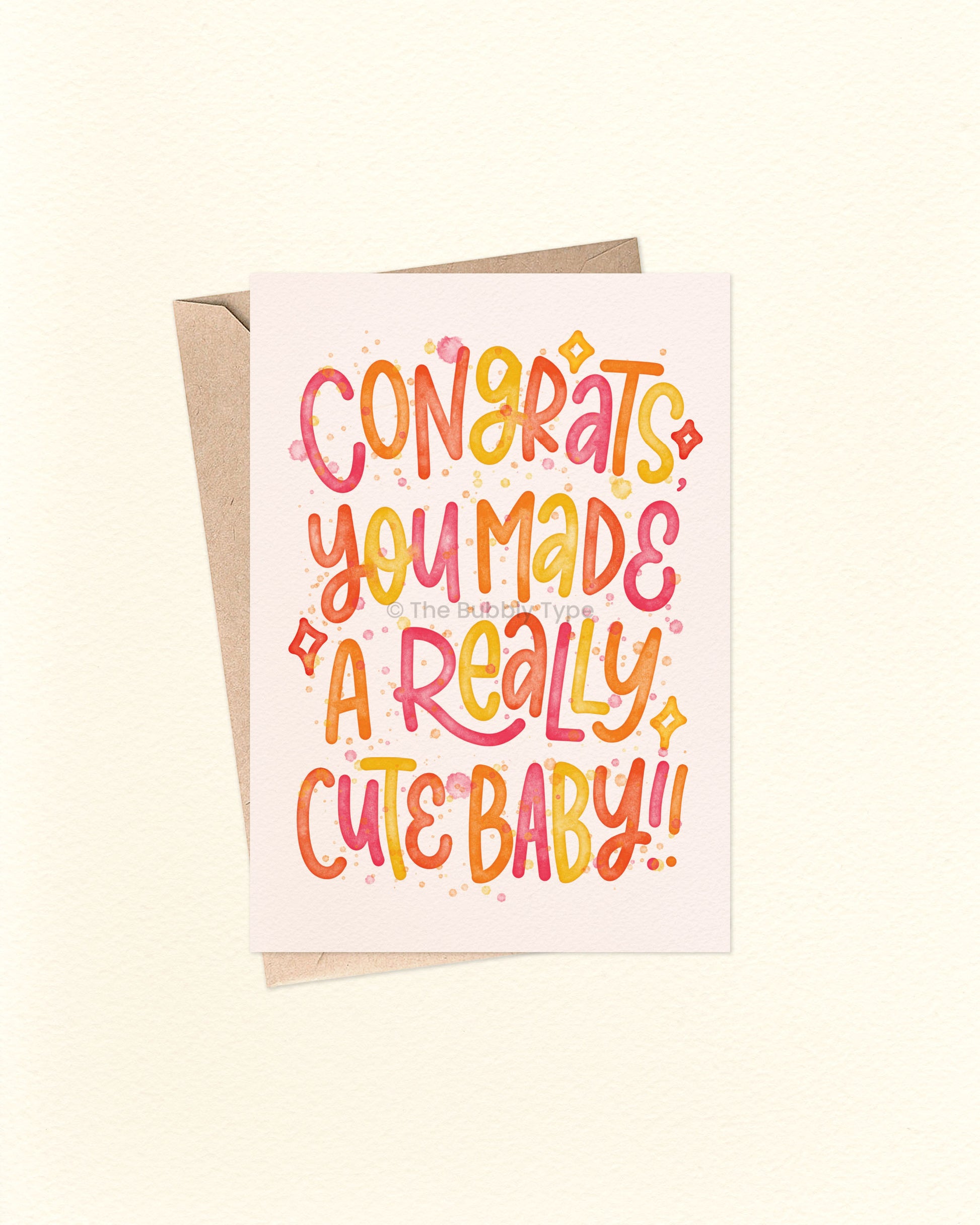 Front of A6 greeting card featuring playful hand-lettered text that reads, “Congrats you made a really cute baby” in warm watercolour tones including red, orange, and yellow. Surrounded by fun starbursts and paint splashes, this cheerful Australian made card by The Bubbly Type is perfect for new parents. Set against a soft cream background and shown with a brown kraft envelope.