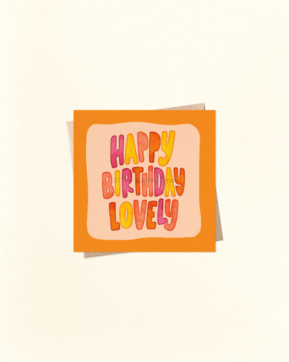 Front of 10cm square birthday card featuring hand-lettered watercolour text that reads “Happy Birthday Lovely” in the centre, surrounded by an orange border and lighter orange background. Paired with a brown kraft envelope. Australian made card by The Bubbly Type – a bright and cheerful birthday greeting for someone special.