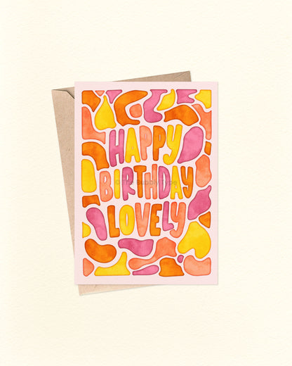 Front of A6 birthday card featuring free-flowing watercolour blob shapes in warm colours like pink, orange, and yellow, surrounding the hand-lettered message “happy birthday lovely.” A joyful and vibrant card by The Bubbly Type, perfect for celebrating someone special. Displayed with a brown kraft envelope.