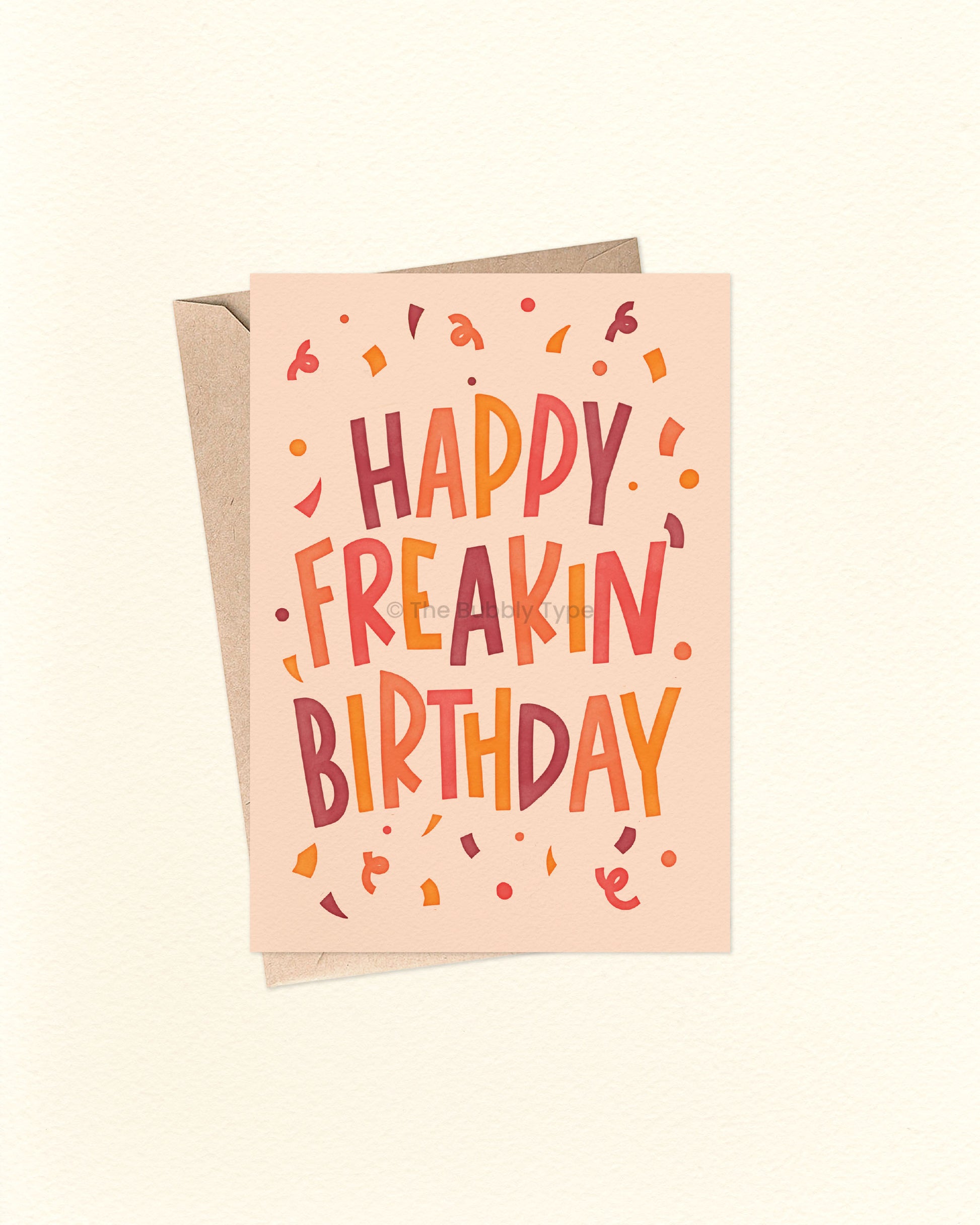 Front of A6 birthday card featuring bold blocky hand-lettered text that reads “Happy Freakin' Birthday” surrounded by colourful confetti. The design uses warm, bright colours like orange, yellow, warm purple, and cream. A fun and cheeky birthday card from The Bubbly Type, perfect for friends or anyone who loves bold vibes. Shown with a brown kraft envelope.