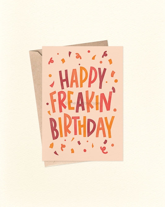 Front of A6 birthday card featuring bold blocky hand-lettered text that reads “Happy Freakin' Birthday” surrounded by colourful confetti. The design uses warm, bright colours like orange, yellow, warm purple, and cream. A fun and cheeky birthday card from The Bubbly Type, perfect for friends or anyone who loves bold vibes. Shown with a brown kraft envelope.
