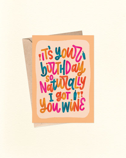 Front of A6 birthday card featuring a playful hand-lettered message that reads “It’s your birthday so naturally I got you wine” in bold, bright colours with a watercolour finish. The text is in a loopy, cursive style over a pale orange background with a deeper orange border. A cheeky, fun birthday card from The Bubbly Type, shown with a brown kraft envelope.