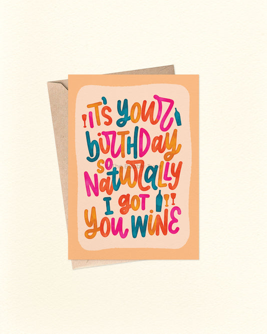 Front of A6 birthday card featuring a playful hand-lettered message that reads “It’s your birthday so naturally I got you wine” in bold, bright colours with a watercolour finish. The text is in a loopy, cursive style over a pale orange background with a deeper orange border. A cheeky, fun birthday card from The Bubbly Type, shown with a brown kraft envelope.