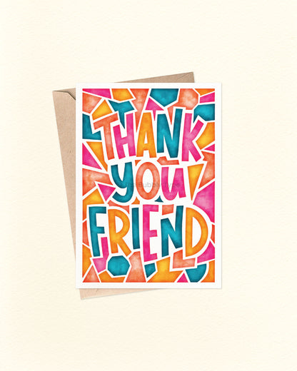 Front of A6 greeting card featuring bold hand-lettered block text that reads, “Thank You Friend” in vibrant watercolour shades of orange, pink, yellow, and teal blue. Surrounded by playful abstract shapes on a soft background, this card by The Bubbly Type is a joyful way to show appreciation to a friend. Displayed with a brown kraft envelope.