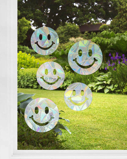 Five smiley face sun catchers in various sizes stuck on a window, Australian made rainbow maker decals creating colourful light reflections, cute and cheerful window stickers for kids' rooms or home decor.