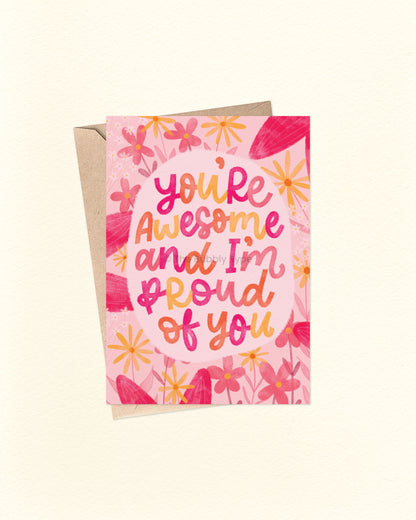 Front of A6 greeting card featuring a vibrant watercolour floral design with pink and yellow flowers surrounding a hand-lettered quote that reads, “You’re awesome and I’m proud of you.” Set on a soft pink background, this uplifting Australian made card by The Bubbly Type is perfect for graduation, new jobs, promotions, or any achievement worth celebrating. Shown with a brown kraft envelope.