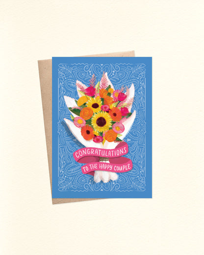 Front of A6 card designed for weddings or engagements. The background is a soft blue with fine white line pattern details. A vibrant watercolour-style bouquet takes centre stage, featuring sunflowers, hot pink and orange roses, pink peonies, yellow roses, and green foliage. The flowers are wrapped in a white paper wrap, with a pink ribbon banner at the bottom that reads: “Congratulations to the happy couple.” Shown with a kraft brown envelope.
