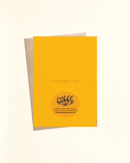 Back of the card with a yellow background featuring The Bubbly Type logo and card details. Shown with a kraft brown envelope. Printed on 100% recycled paper in Australia. Shown with a kraft brown envelope.