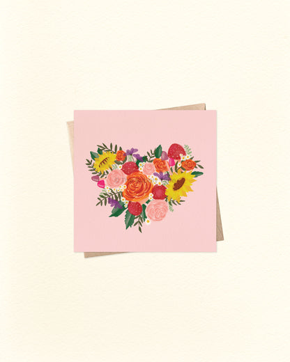 Front of 10cm square greeting card featuring a heart-shaped illustration made up of whimsical mushrooms and flowers in a watercolour style, set against a pale pink background. Paired with a brown kraft envelope. Australian made card by The Bubbly Type – perfect for love notes, friendship, or nature lovers. This card says "I Love You" or "Happy Mother's Day" or "Congratulations on your Wedding" or suits whatever occasion you like.