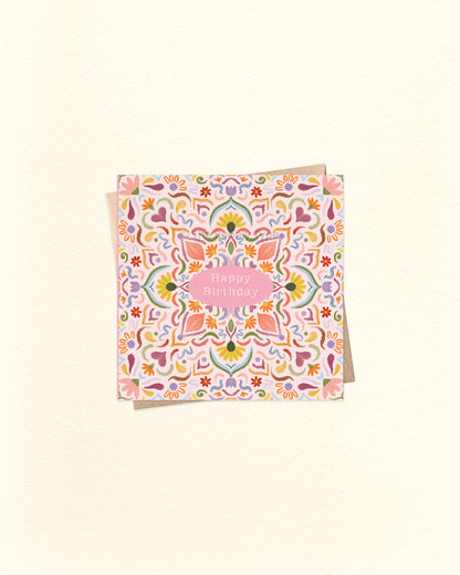 Front of 10cm square birthday card featuring a watercolour tile pattern in warm, vibrant colours – including pink, orange, blue, and purple. “Happy Birthday” is written in small text at the centre. Paired with a brown kraft envelope. A colourful and artistic Australian made birthday card by The Bubbly Type.