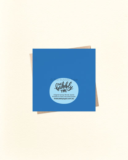 Back of the new baby greeting card with deep blue background, showing The Bubbly Type logo and print details. Printed in Australia on sustainably sourced cardstock. Shown over a kraft brown envelope.