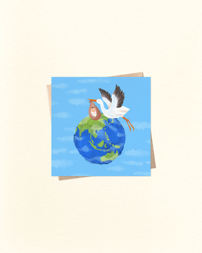 Front of 10cm square greeting card featuring a watercolour-style illustration of the Earth with a white stork flying across, carrying a baby bundle. Paired with a brown kraft envelope. Australian made card by The Bubbly Type – a sweet and thoughtful way to welcome a newborn.