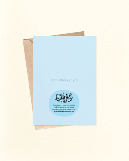 Back of the card with a matching blue background, featuring The Bubbly Type logo and card details. Displayed with a kraft brown envelope. Designed and printed in Australia on sustainable card stock.