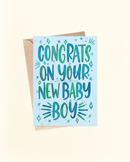 Front of A6 greeting card featuring hand-lettered watercolour text that reads, “Congrats on your new baby boy” in shades of blue, green, and teal. The message is surrounded by whimsical stars and line accents on a bold blue background. A cheerful Australian made card by The Bubbly Type, perfect for celebrating the arrival of a baby boy. Shown with a brown kraft envelope.