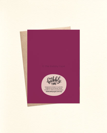 Back of the card with a rich deep purple background featuring The Bubbly Type logo and card details. Shown with a kraft brown envelope.

