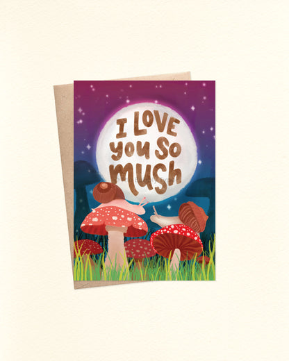 Front of A6 greeting card featuring a whimsical watercolour illustration of two snails sitting atop red-capped mushrooms, reaching out to each other. Behind them is a large glowing white moon with hand-lettered brown text that reads: “I love you so mush.” The background is a starry twilight sky in deep blue and purple hues. Shown with a brown kraft envelope.