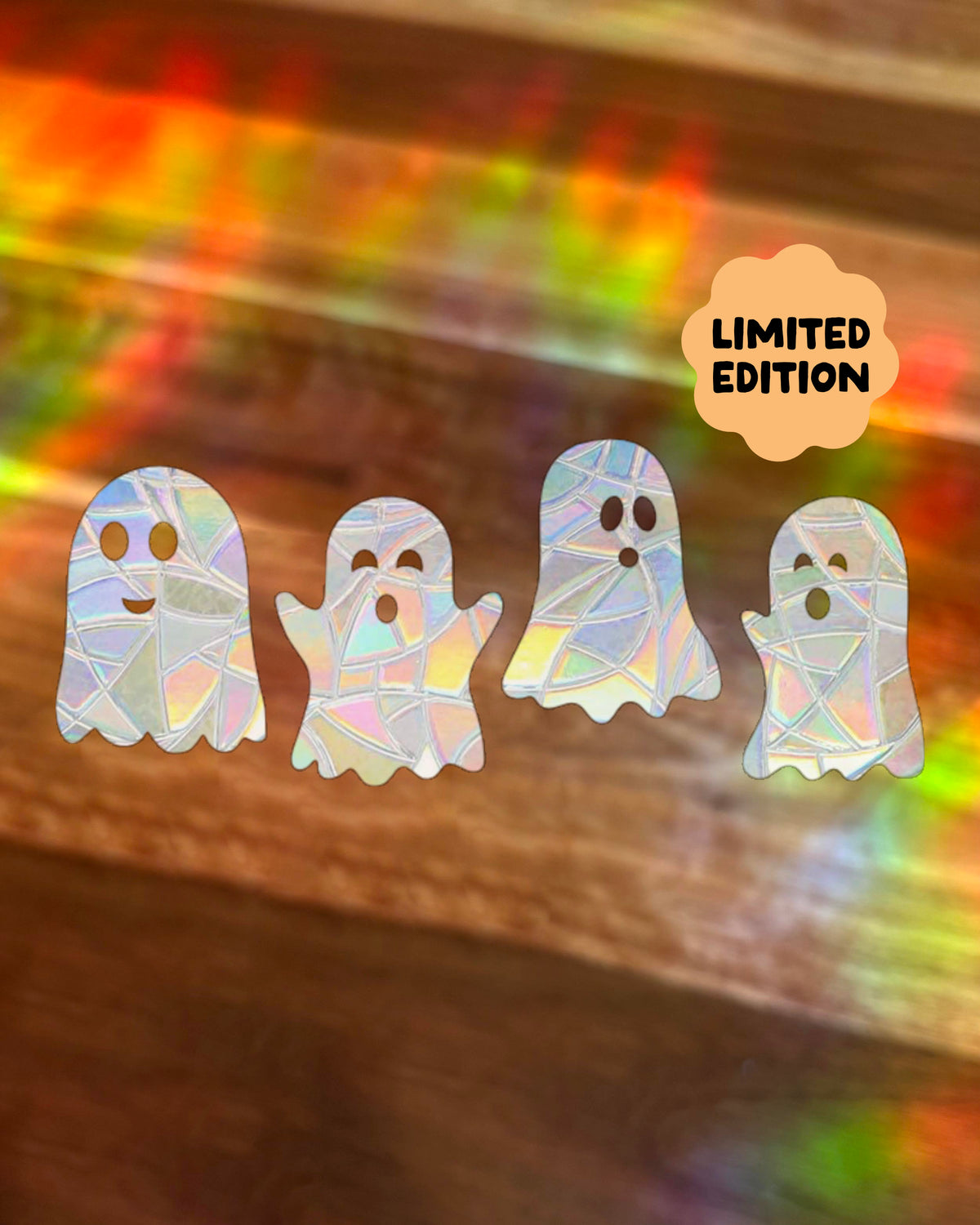 Four ghost-shaped window stickers with a holographic iridescent finish are arranged on a blurred rainbow-lit surface. An orange cloud badge in the top right reads “LIMITED EDITION.