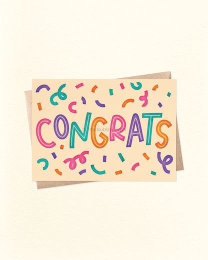 Front of A6 congratulations card featuring bold block lettering that spells out “CONGRATS” in pink, purple, green, and orange, surrounded by colourful confetti. Set on a pale yellow cream background and paired with a brown kraft envelope. A bright and cheerful Australian made card by The Bubbly Type – perfect for graduations, new jobs, engagements, and more.
