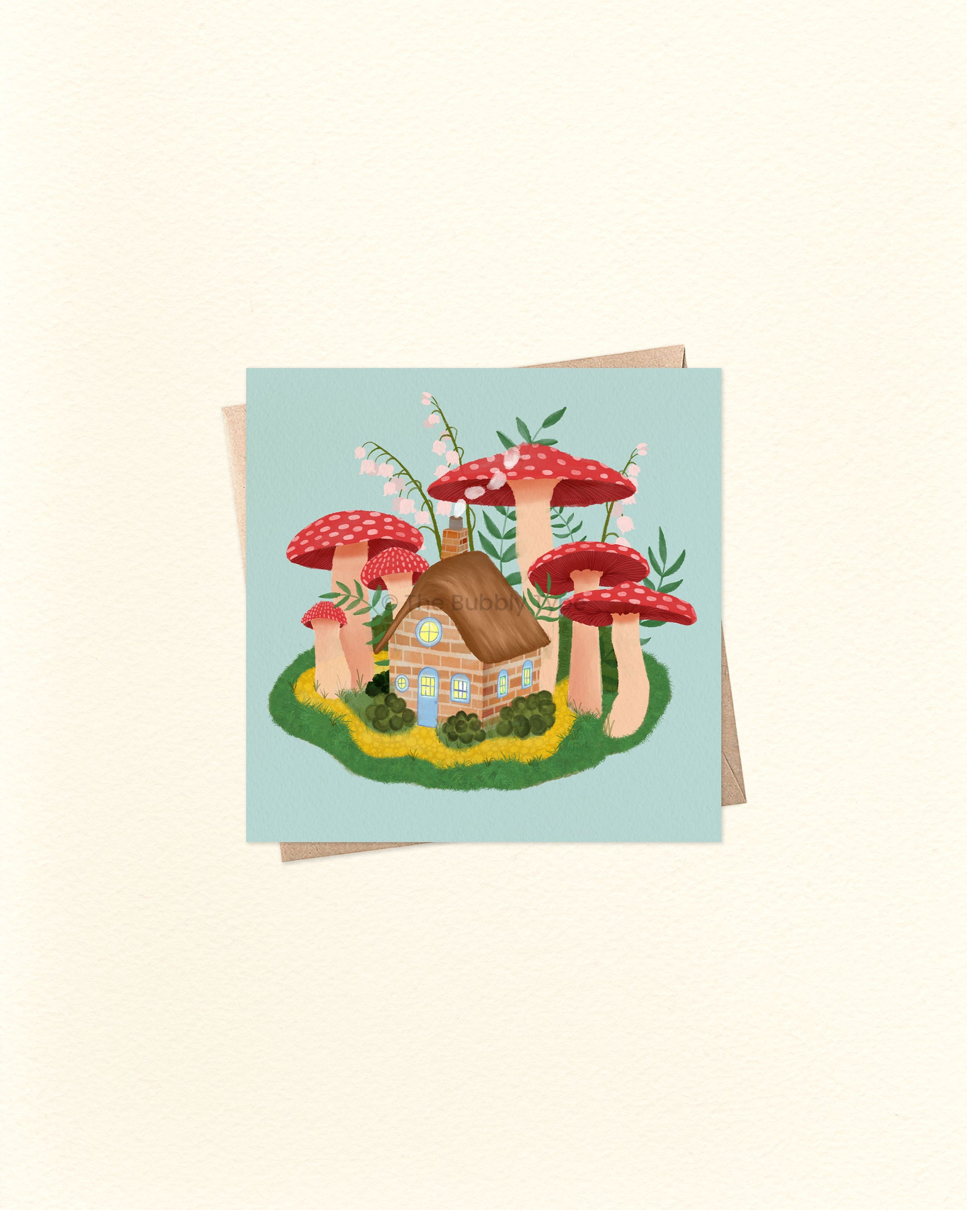 Front of square greeting card featuring a whimsical illustration of a cottage surrounded by mushrooms, paired with a brown kraft envelope. 10cm x 10cm card by The Bubbly Type – Australian made and blank inside. Perfect for fairytale lovers, nature fans, or a magical little note.