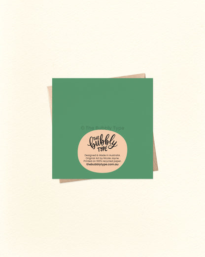Back of the 10cm square Mushroom Cottage card with green background, showing The Bubbly Type logo and printed details, placed over a kraft brown envelope. Designed and printed in Australia on eco-friendly cardstock.